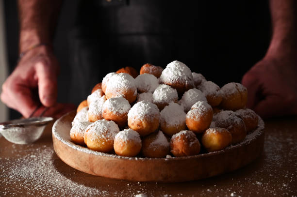 istock Man sprinkles powdered sugar onBaked castagnole. Round biscuits with sugar for the carnival of Venice. Traditional sweet pastries during the carnival period in italy. horizontal photo.  Copy space. 1302334204