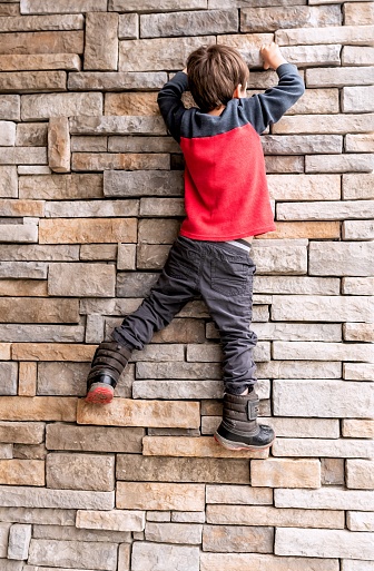 Caucasian Little boy climbing a brick wall
