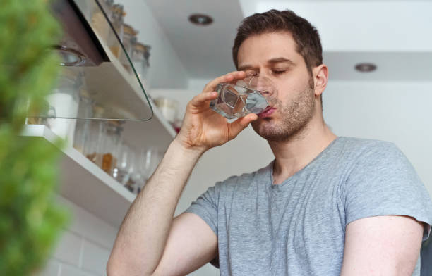 istock Unshaven man drinks water from a glass in the kitchen. 1302337849