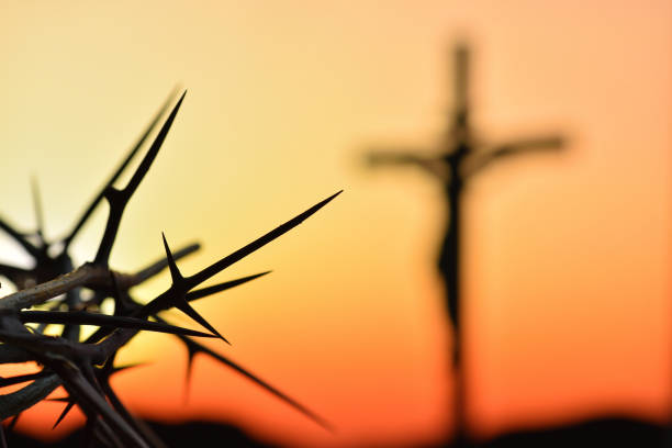 Crown of thorns of Jesus Christ against silhouette of catholic cross at sunset background stock photo