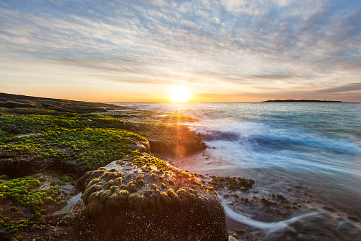 Ocean water flowing over rocks and beach with golden sunrise