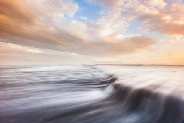 Ocean waves flowing over rocks at sunrise with pink storm clouds