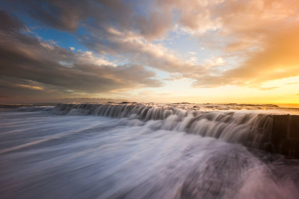 Ocean waves flowing over rocks at sunrise with orange and gold storm clouds
