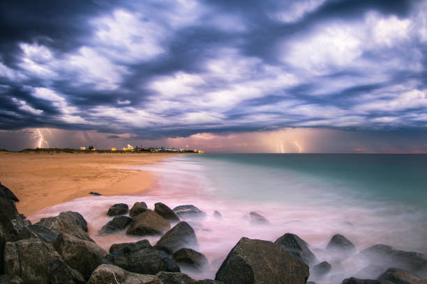 istock Ocean waves flowing over rocks and beach at sunset with storm clouds and lightning 1302340435
