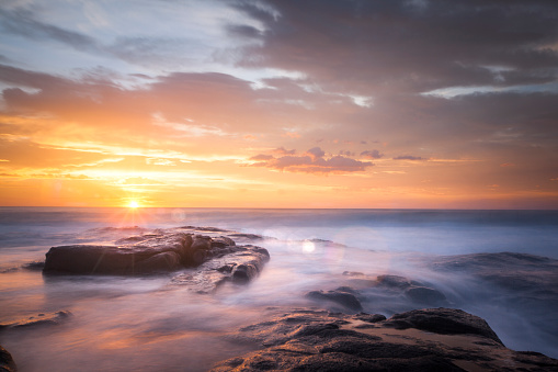 Ocean waves flowing over rocks at sunrise with orange and gold storm clouds