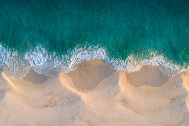 luftaufnahme von weißer sandstrandküste und wirbelnden wellen mit blaublauem ozean - green sky water wave stock-fotos und bilder