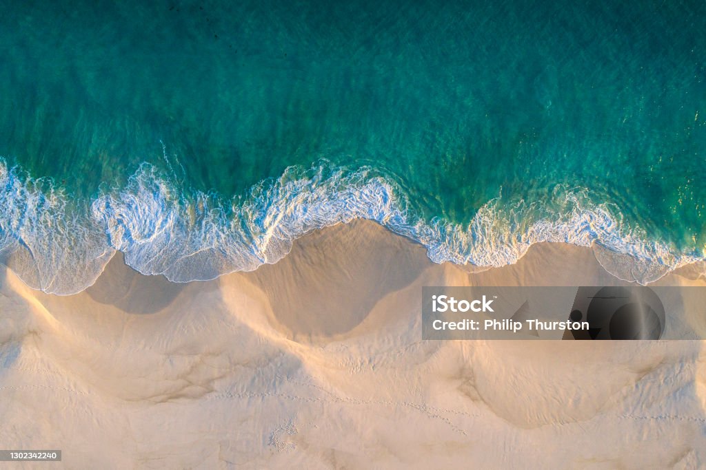 Aerial view of white sand beach coastline and swirling waves with teal blue ocean Sea Stock Photo