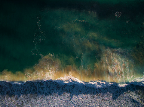Directly above aerial view of storm wave breaking on the beach in early morning light