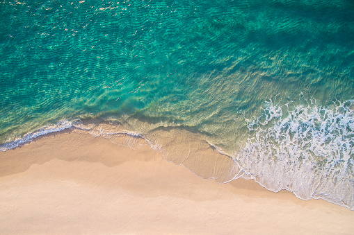 Clean ocean waves breaking on white sand beach with turquoise emerald coloured water. Aerial view. Perfect weather.