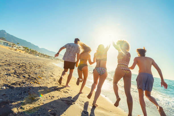 grupo de amigos corriendo y saltando al océano al atardecer. - marbella fotografías e imágenes de stock