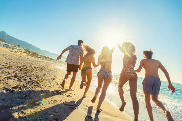 日没時に海に飛び込む友人のグループ。 - beach men party bikini ストックフォトと画像