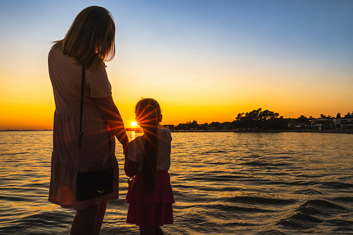 Mother and daughter holding hands, admiring beautiful sunset at Adriatic Sea beach
