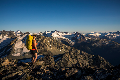 Strong female with heavy backpack standing at top of mountain in Whistler backcountry.