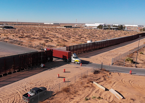 Following Drone Clip of a Container Semi-Truck Passing Through the US Mexico Border Wall and Going to US Customs To Import Goods