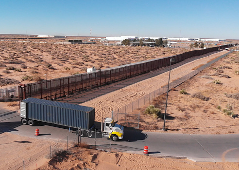 Following Drone Clip of a Container Semi-Truck Passing Through the US Mexico Border Wall and Going to US Customs To Import Goods