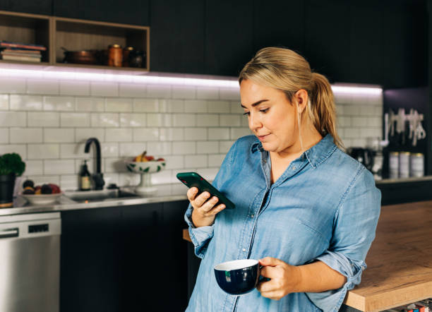 istock Woman in Kitchen with Smart phone and coffee cup 1302347952