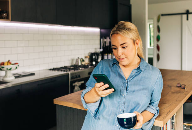 istock Woman in Kitchen with Smart phone and coffee cup 1302347984