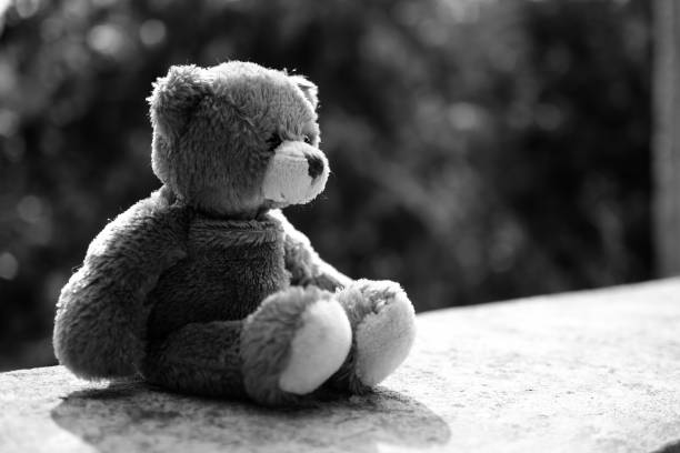 istock Broken heart concept. black and white image of teddy bear sad face sitting on cement wall. for isolation, loneliness, abandoned child, conceptual. 1302349849