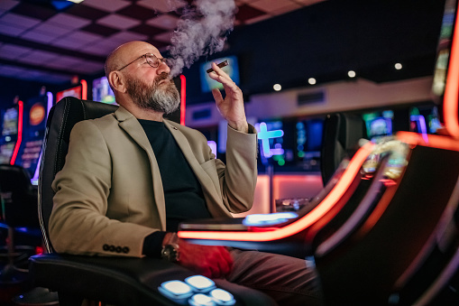 Senior men using slot machine to gamble in night club, having difficulties to make money, he is losing