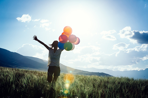 Cheering young woman running on sunset grassland with colored balloons