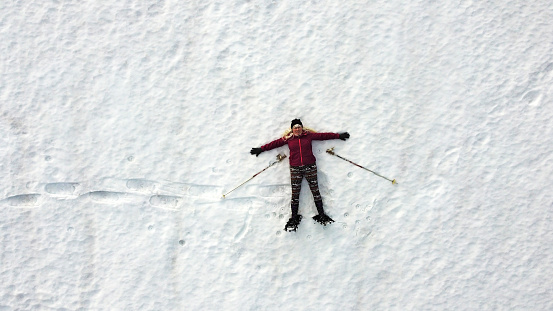 Aerial drone shot of woman snowshoeing lying in snow