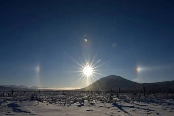 Ice crystals in the atmosphere reflect sunlight to form a halo around the sun. The two bright spots to the left and right of the sun are called sundogs.