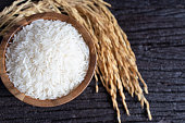 White rice (Thai Jasmine rice) in wooden bowl and paddy rice on dark wooden texture background.