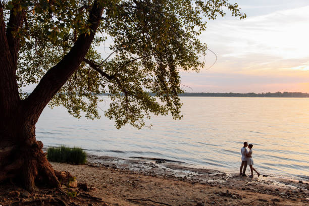 istock Two young people hug under an old tree by the river. 1302370044