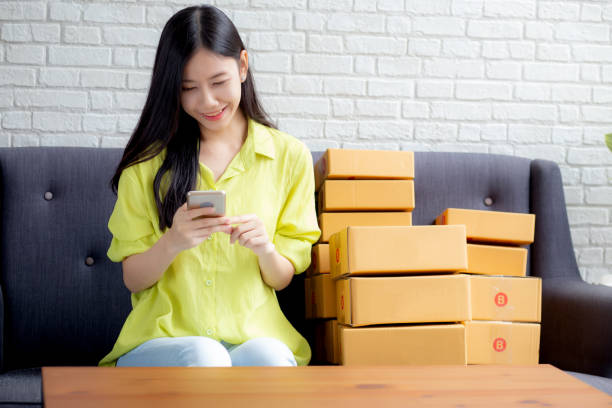 istock Young asian woman is entrepreneur check order from smartphone with customer while purchase online, logistic and delivery, online shopping, female is seller of business SME, merchant looking phone. 1302373187