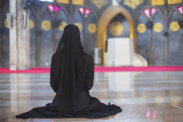 молодая мусульманка в черном платье сидит одна в мечети, вид сзади. - arabia architecture asia rear view стоковые фото и изображения