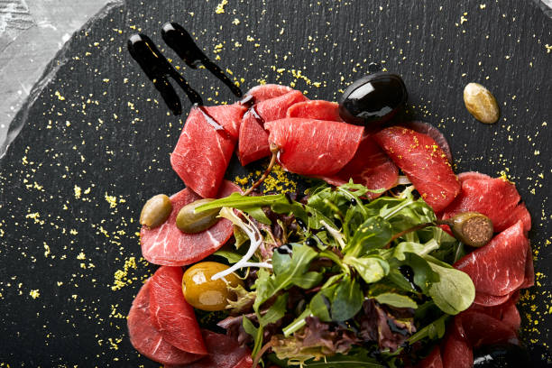 carpaccio di manzo con rucola su piatto nero, cucina tradizionale italiana. tasto scuro, spazio di copia - beef carpaccio foto e immagini stock