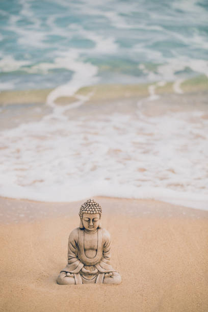 istock Buddha stone figure sitting on the seashore on the beach with a coming water-wave 1302382021