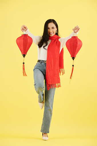 Excited pretty young Asian woman in warm clothes showing silk red paper lanterns for Chinese New Year celebration