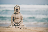 Close up of a Buddha stone figure sitting on the seashore in front of the slightly rough sea