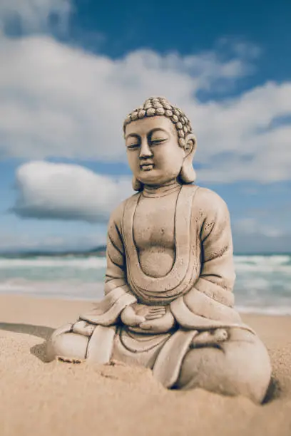 Buddha stone figure sitting on the seashore in front of the sea Selective focus and added grain. Part of a series.