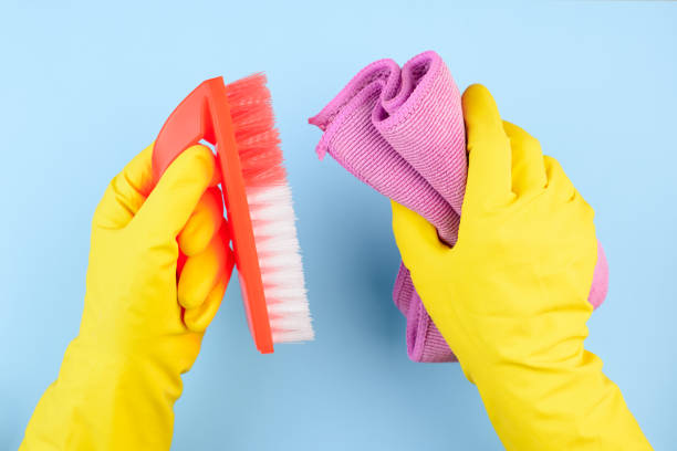 istock Hands in yellow gloves with brush and rag on blue background 1302385973