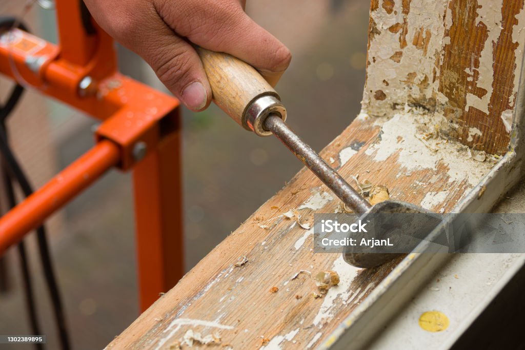 House renovation. A painter removing old paint with a scraper. Wood - Material Stock Photo