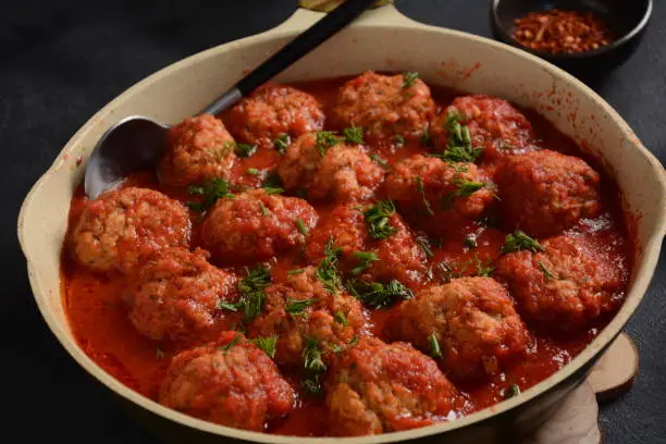 Boulettes de Poisson, Fried Fish Balls in Tomato Sauce in a white dish on a concrete table with ingredients