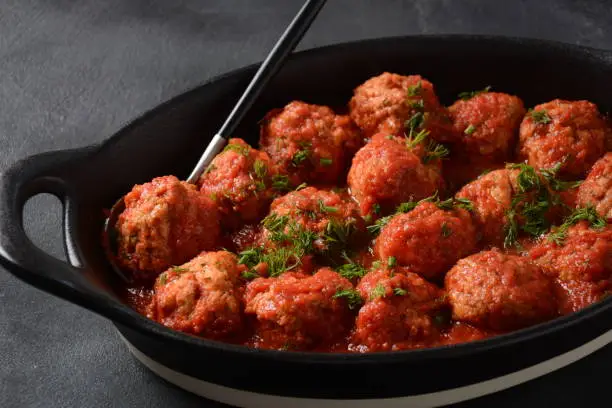 Boulettes de Poisson, Fried Fish Balls in Tomato Sauce in a black dish on a concrete table with ingredients