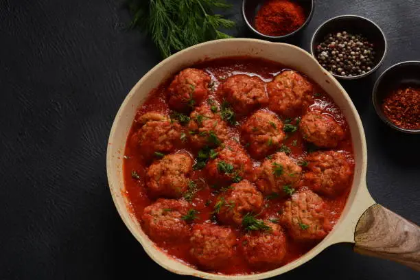 Boulettes de Poisson, Fried Fish Balls in Tomato Sauce in a white dish on a concrete table with ingredients