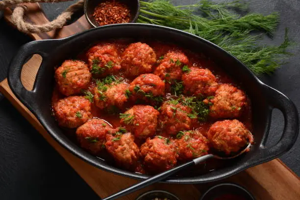 Boulettes de Poisson, Fried Fish Balls in Tomato Sauce in a black dish on a concrete table with ingredients