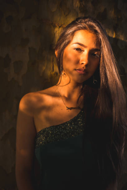 istock A young Latina brunette leaning against a tree with a slight light on her face. Portrait with a sweet and sensual look looking sideways, vertical photo 1302394628