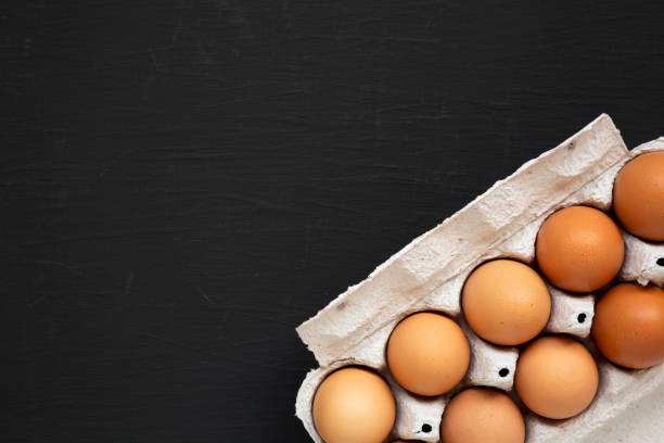 istock Raw Brown Eggs in a paper box on a black background, top view. Flat lay, overhead, from above. Space for text. 1302395167