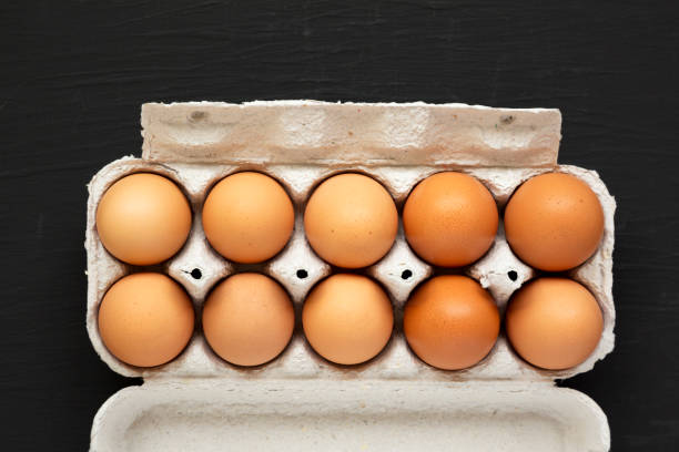 istock Raw Brown Eggs in a paper box on a black background, top view. Flat lay, overhead, from above. 1302395281