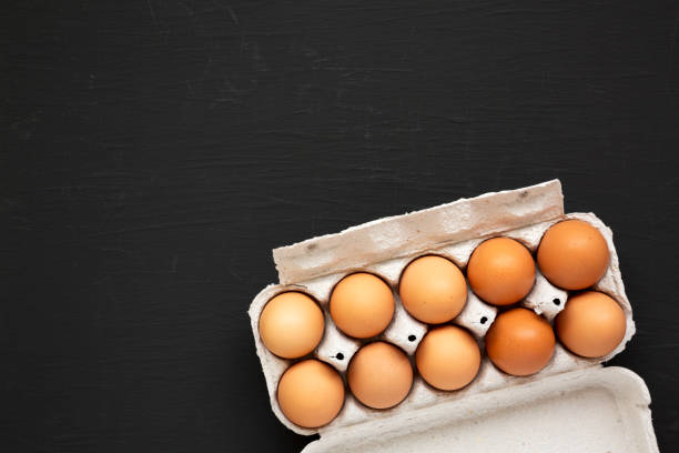 istock Raw Brown Eggs in a paper box on a black surface, top view. Flat lay, overhead, from above. Copy space. 1302395309