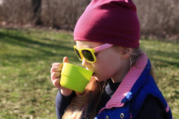 istock Smiling child in colorful clothes drinks tea from bright green reusable cup Spring nature background Eco-friendly picnic 1302396218