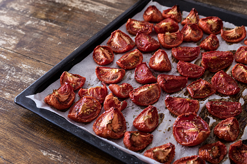 Tomato sliced into halves and fourths, sprinkled with oregano leaves at baking sheet on tray slow roasted - dried