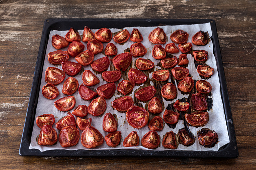 Tomato sliced into halves and fourths, sprinkled with oregano leaves at baking sheet on tray slow roasted - dried
