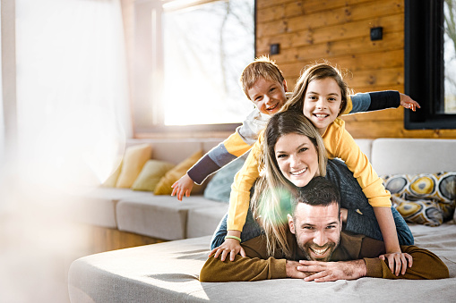 Happy parents and their small kids making human pyramid on sofa in the living room and looking at camera.