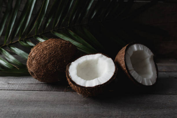 istock Broken coconuts on gray wooden background with palm leaf. White coconut pulp 1302400058